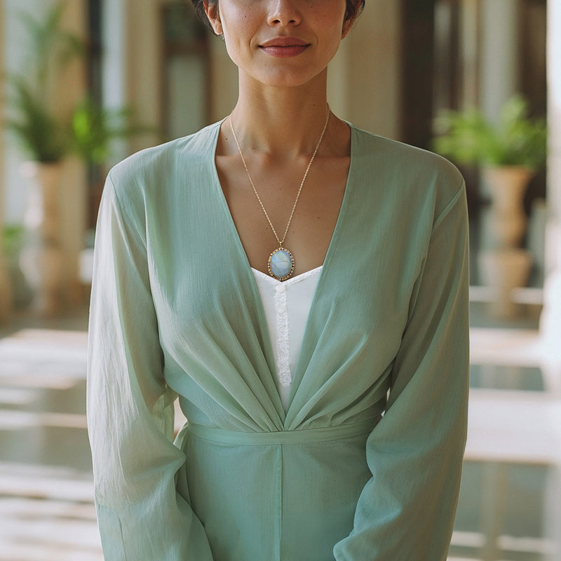 Opal pendant necklace worn on model, oval light blue opal in a gold Greek key frame