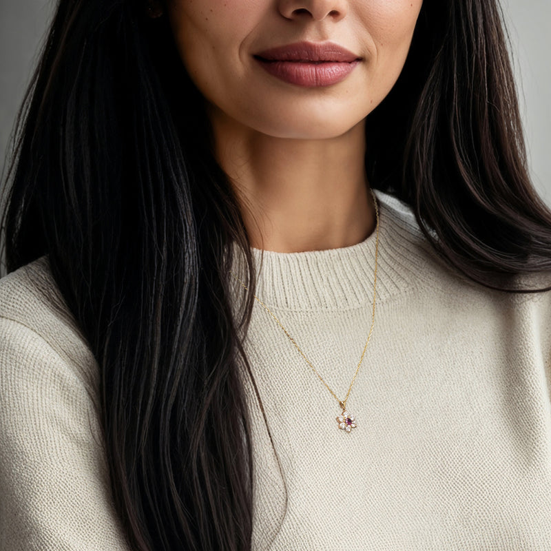 Gold pendant necklace on model with small ruby center and diamond flower design