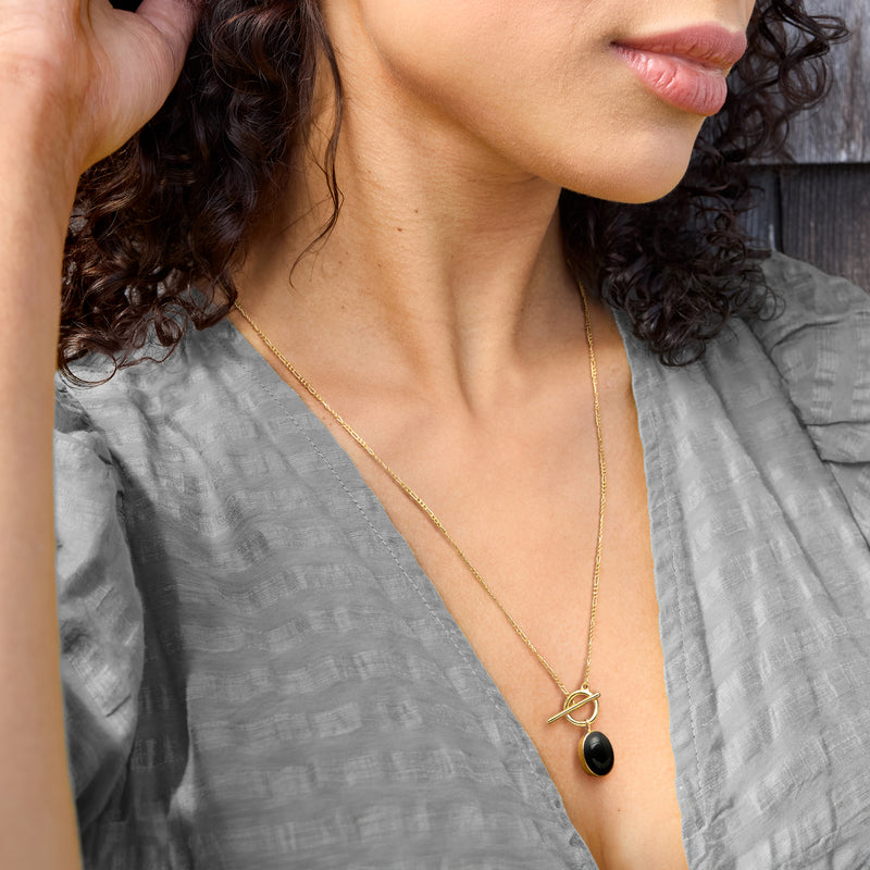 Gold chain necklace with oval black onyx pendant on a V-neck top