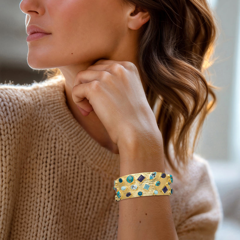 Gold cuff bracelet with multi-color blue and purple gemstones on wrist
