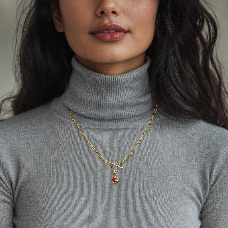 Gold tone necklace chain with small heart ruby charm pendant on chest