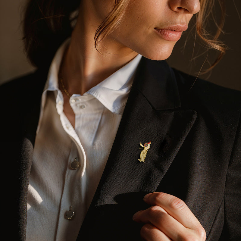 Enamel bird pin with red gem on dark blazer lapel, small colorful design