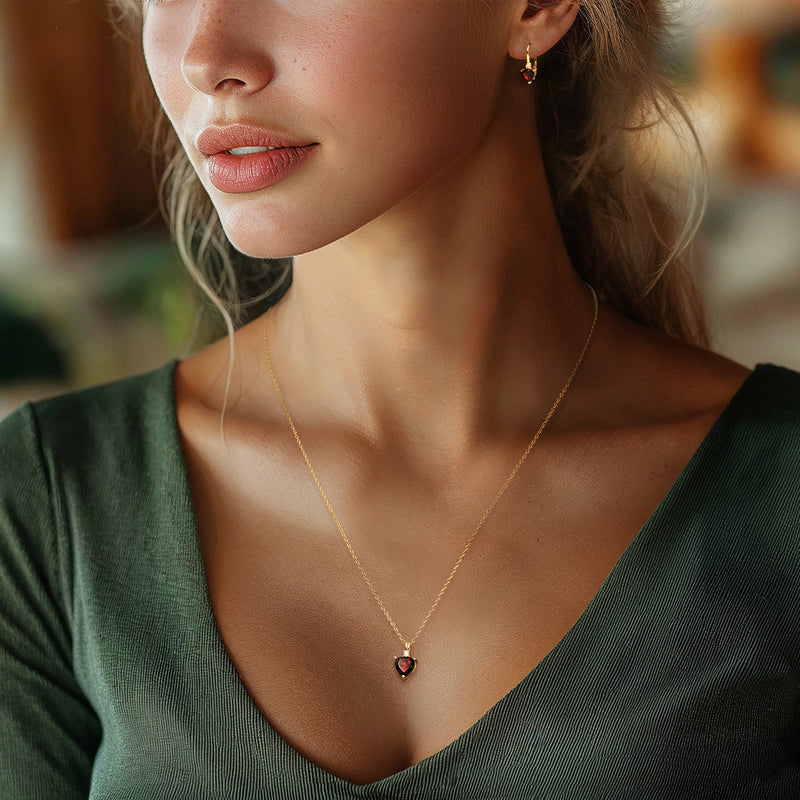 Model wearing gold heart pendant necklace and matching red garnet heart drop earrings