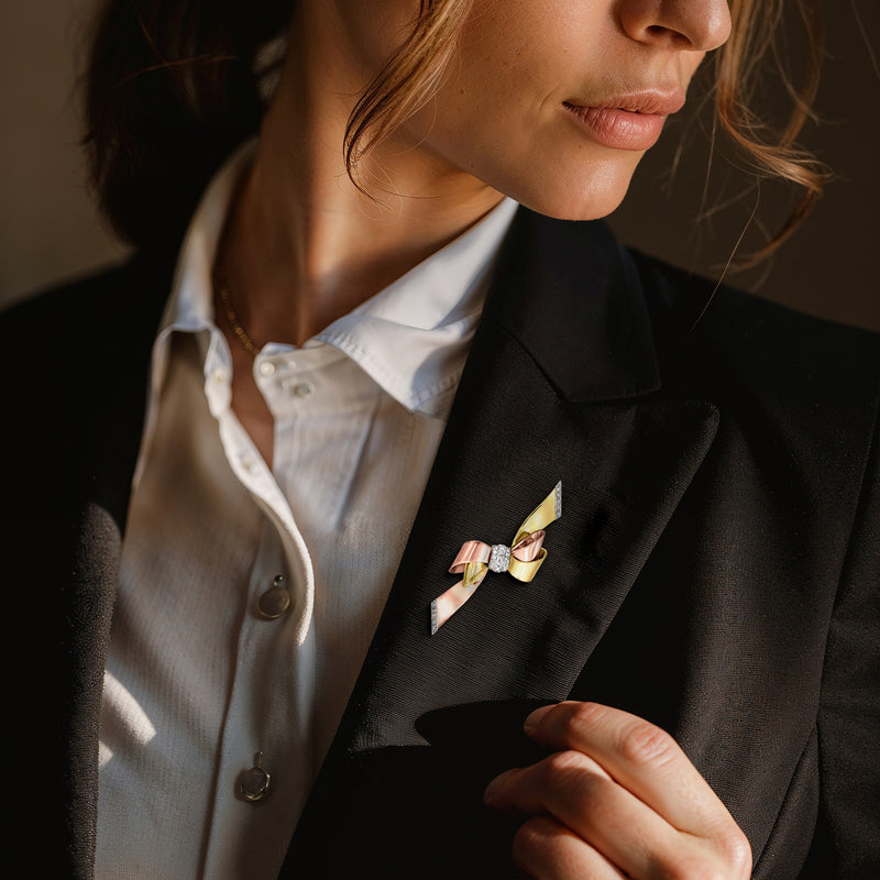 Tri-colored gold bow pin with diamond accents on blazer lapel