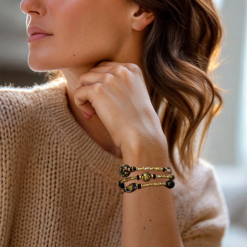 Black and gold glass bead wrap bracelet on wrist, layered with round Murano charms