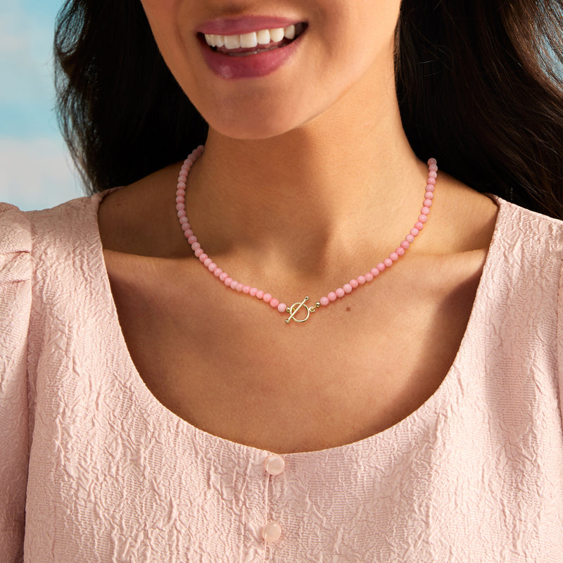 Pink coral beaded necklace with gold-tone toggle clasp and small charm at collar