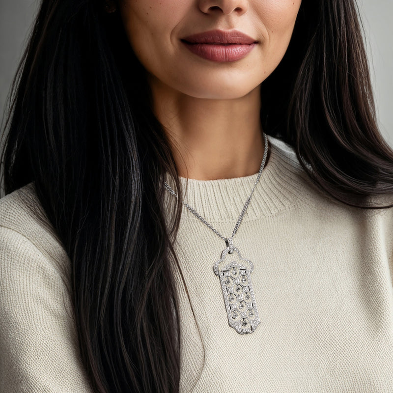 Diamond pendant necklace with rectangular charm and round stones, worn on neckline