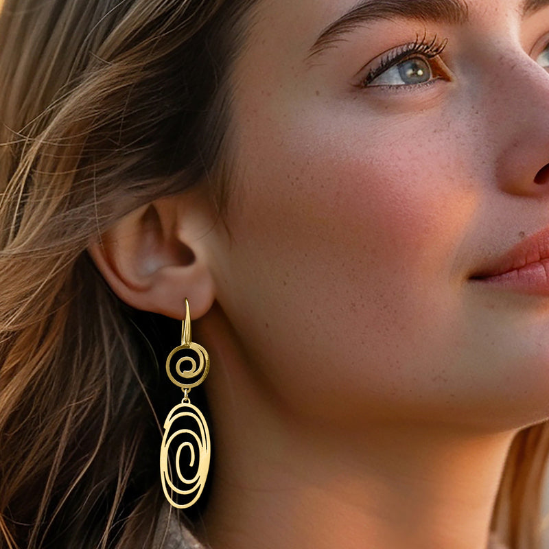 Gold spiral openwork drop earrings on ear with circular swirling oval drop