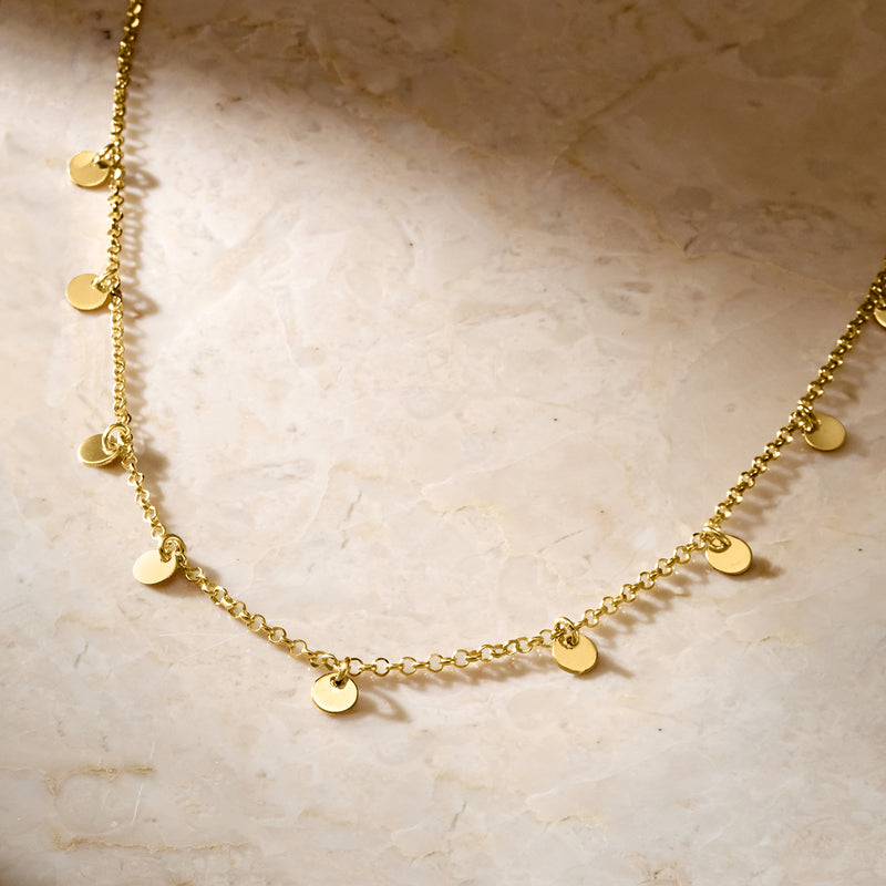 Close-up gold disc station necklace with evenly spaced round charm discs on chain