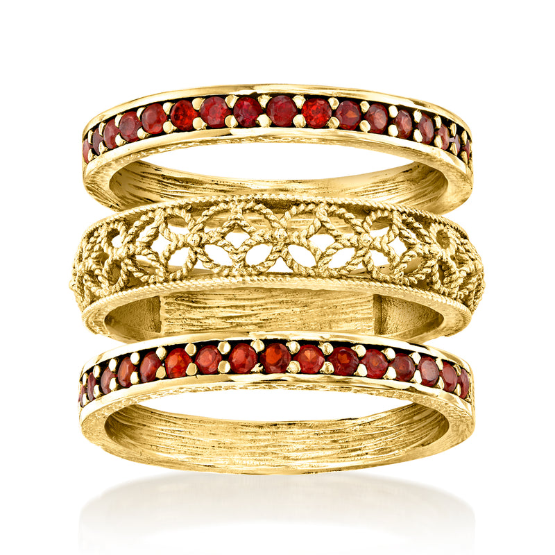 Three stacked gold-tone rings with red garnet stones and scrollwork details