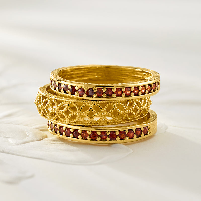 Three gold-tone rings with red garnet stone bands and braided scrollwork centerpiece