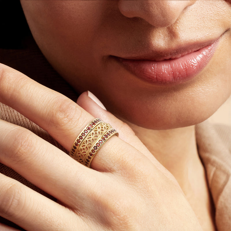 Gold-tone garnet ring with filigree and red stone border on finger