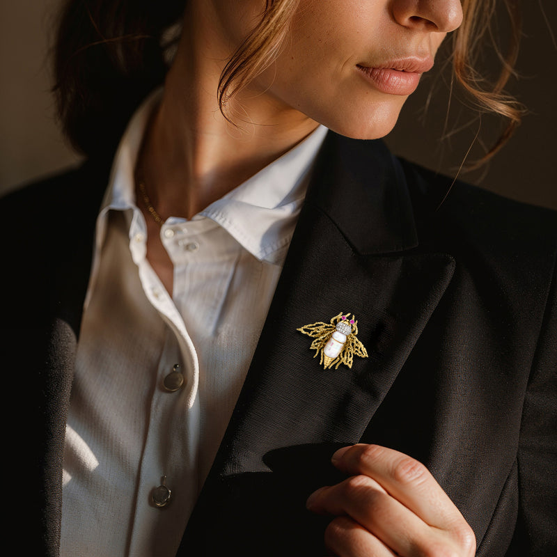 Gold bumblebee lapel pin with pearl center, diamond wings, and ruby eye details on blazer