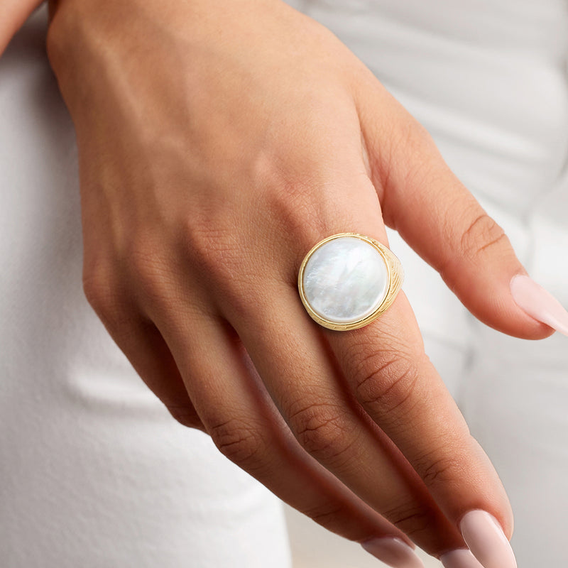 Round mother-of-pearl gold ring worn on finger with white iridescent cabochon
