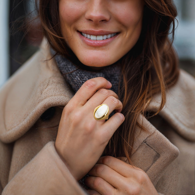 Gold-tone oval mother-of-pearl ring worn on finger, bezel setting visible