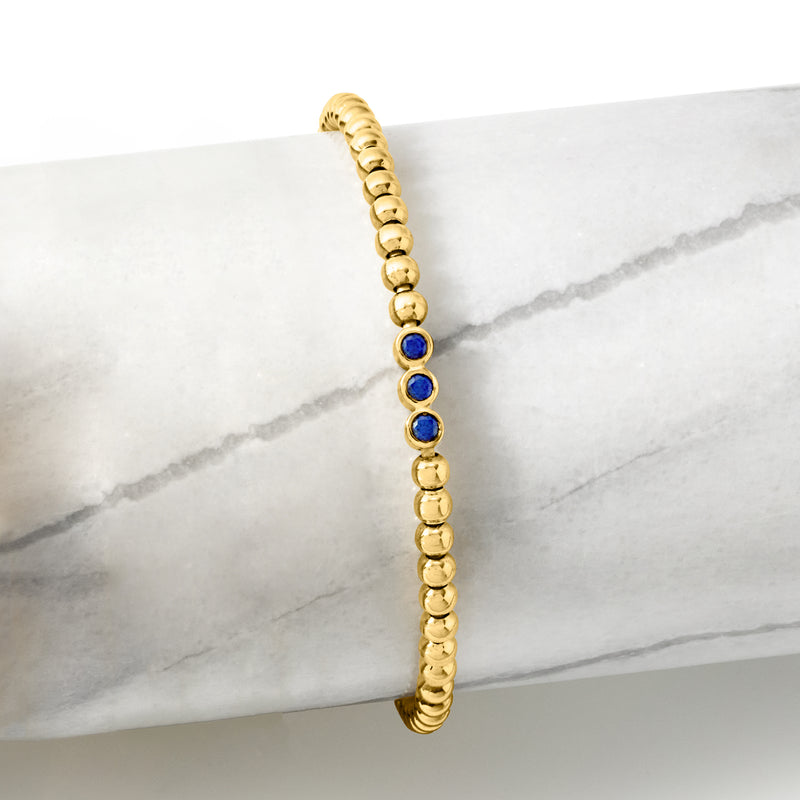 Gold bead stretch bracelet with three blue sapphire stations, close-up