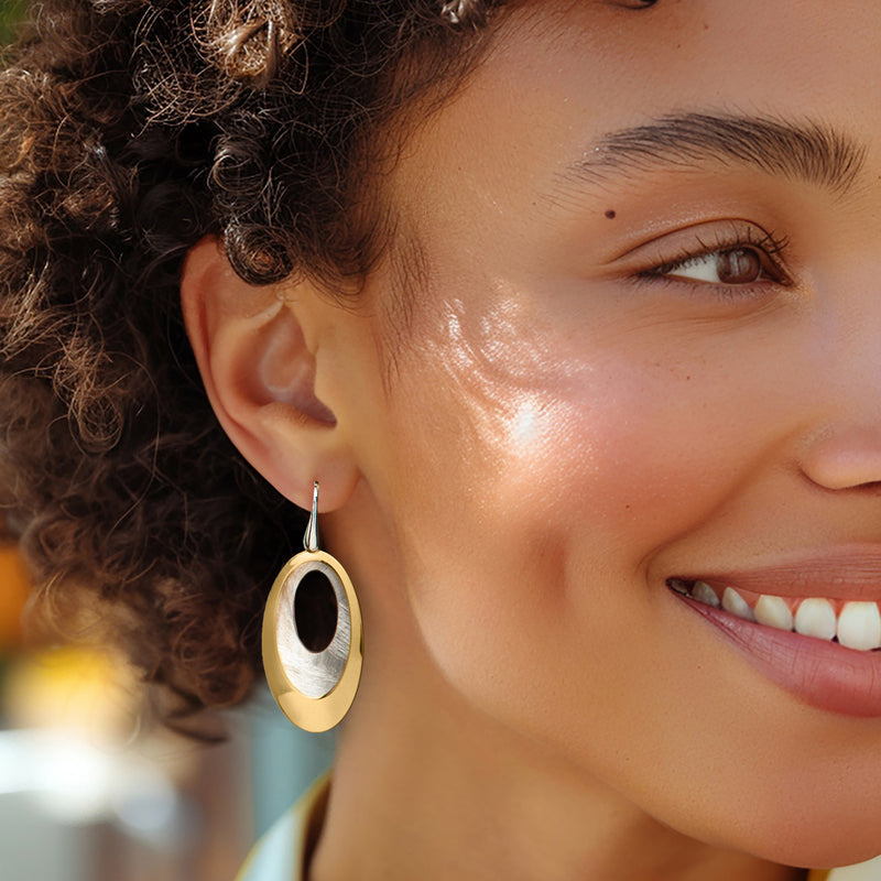 Double-oval drop earrings on ear: gold outer oval and silver inner oval with earwire