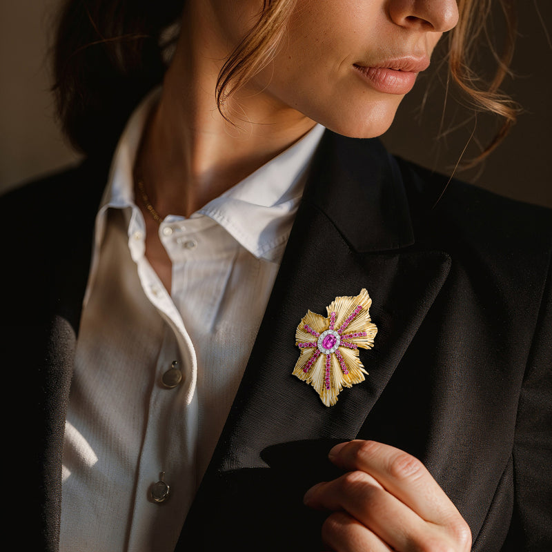Pink gemstone flower pin with gold textured petals on black blazer lapel