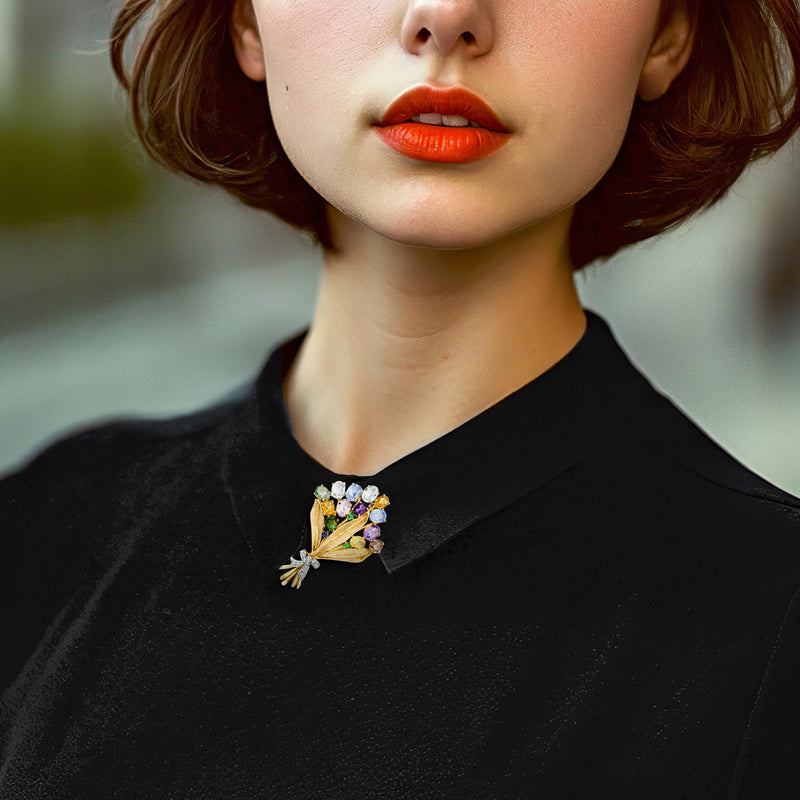 Multicolor gemstone bouquet pin on black top, gold with diamond bow detail.