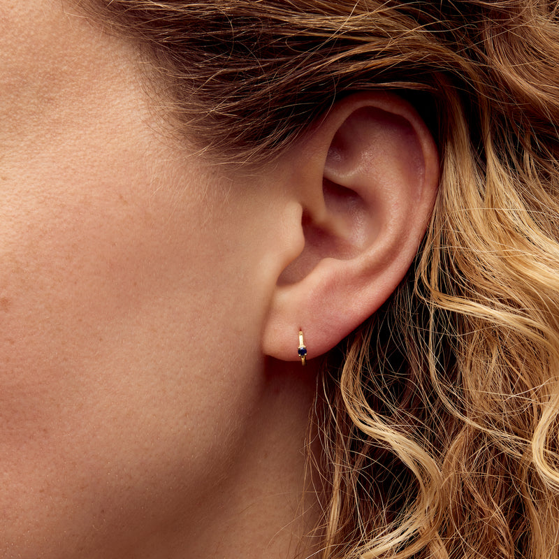 Blue sapphire gemstone in small 14kt yellow gold hoop earring on ear