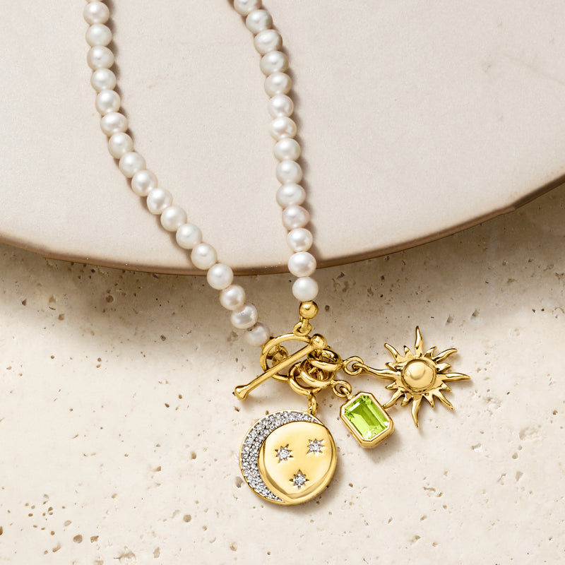 Cultured pearl toggle necklace with gold charm cluster: sun, green stone, heart locket.