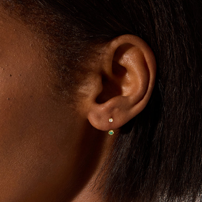 Yellow gold U-hoop earrings with diamond and emerald stones worn on ear