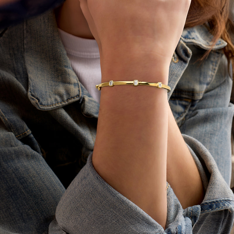Gold station bangle bracelet with three emerald-cut lab diamond accents on wrist