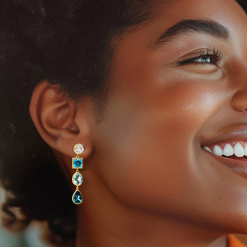 Blue and white topaz drop earrings in gold on model’s ear, three-stone tiers