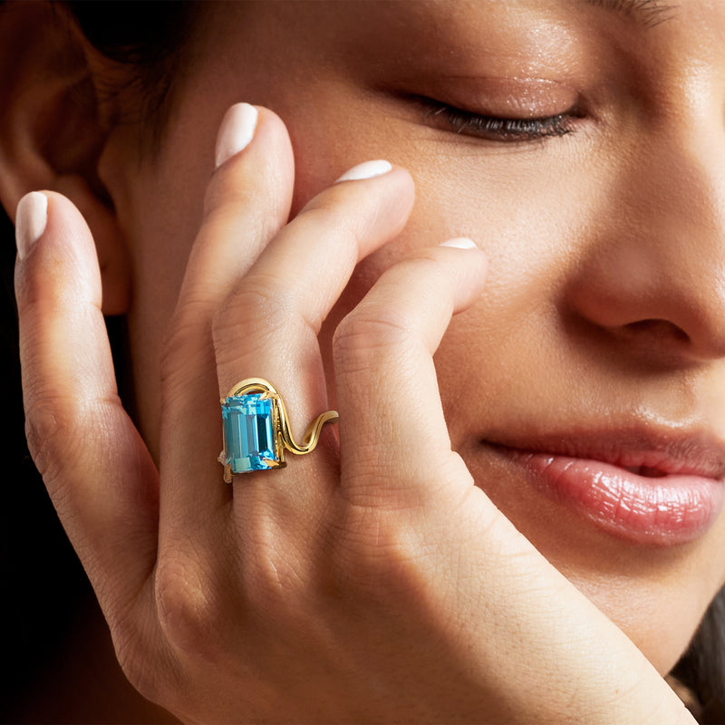Gold-tone ring with cushion-cut blue topaz and diamond accents worn on finger