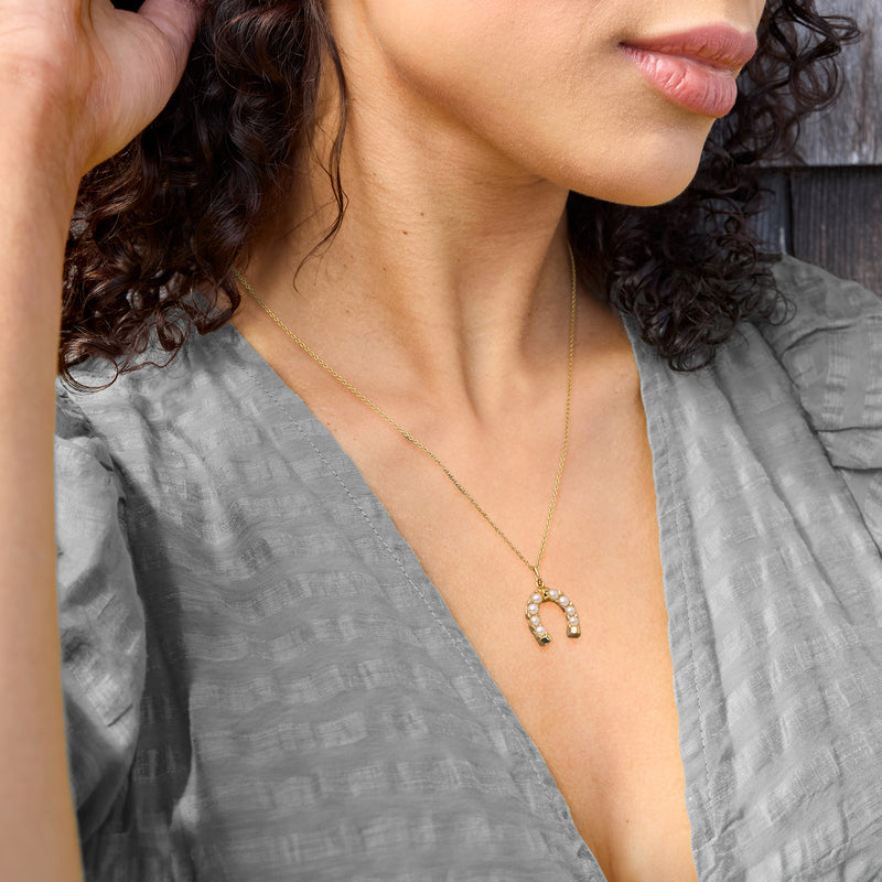 Gold horseshoe pendant necklace with pearl inlay worn on model’s neckline