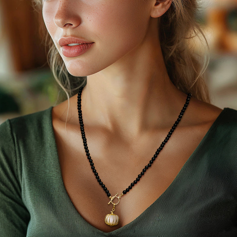 Gold pumpkin charm with white iridescent center on black beaded necklace