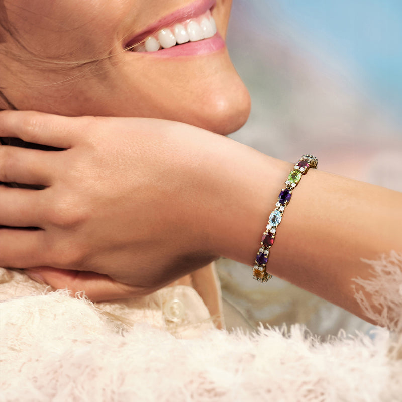 Multi-gemstone bracelet in yellow gold worn on wrist, featuring purple, green, red stones