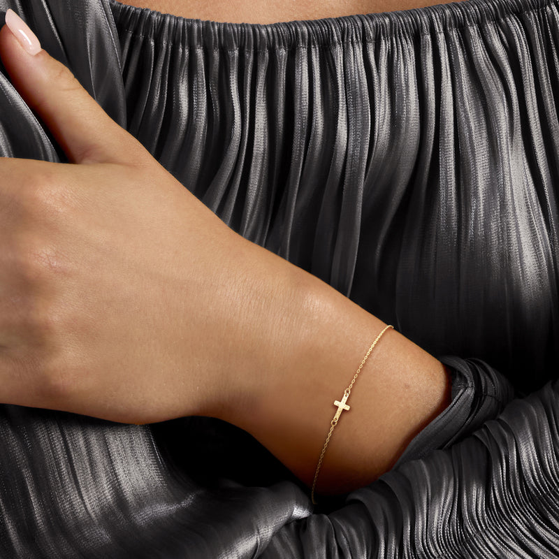 Yellow gold cross charm bracelet worn on wrist, linked chain with small clasp