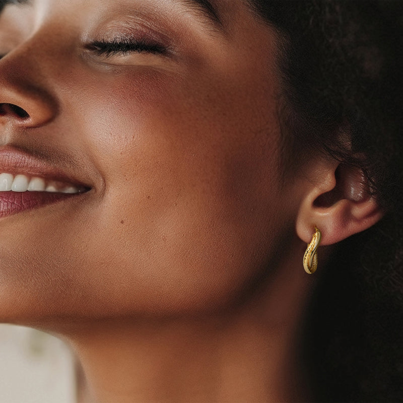 Twisted yellow gold double-oval hoop earrings on ear