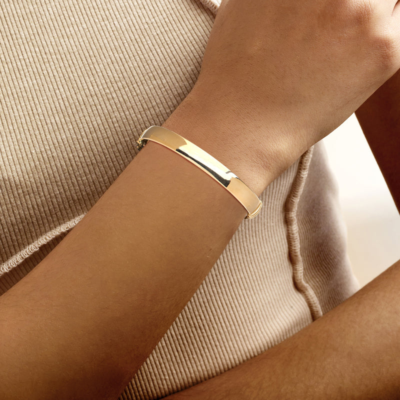 Yellow gold oval bangle bracelet on wrist, smooth hinged design