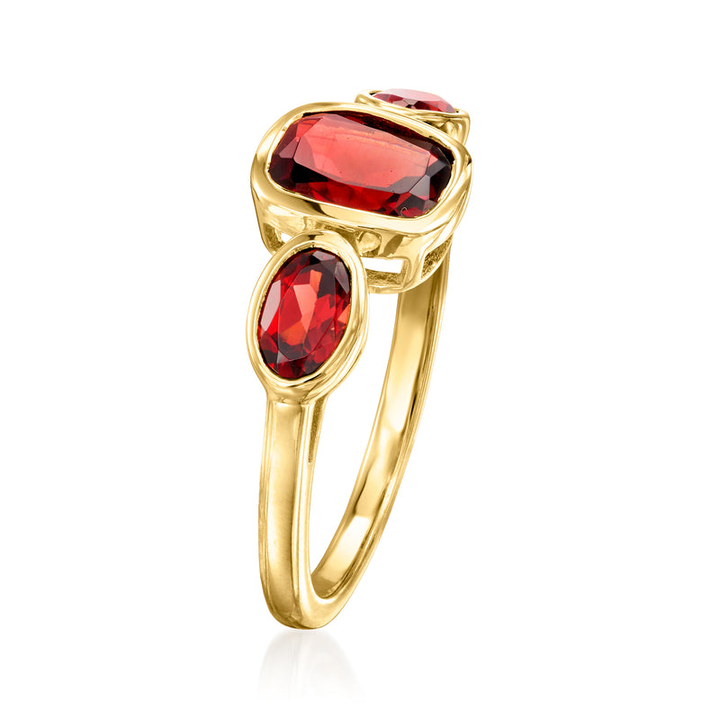 Gold ring featuring red garnet center stone and red side stones in prong settings