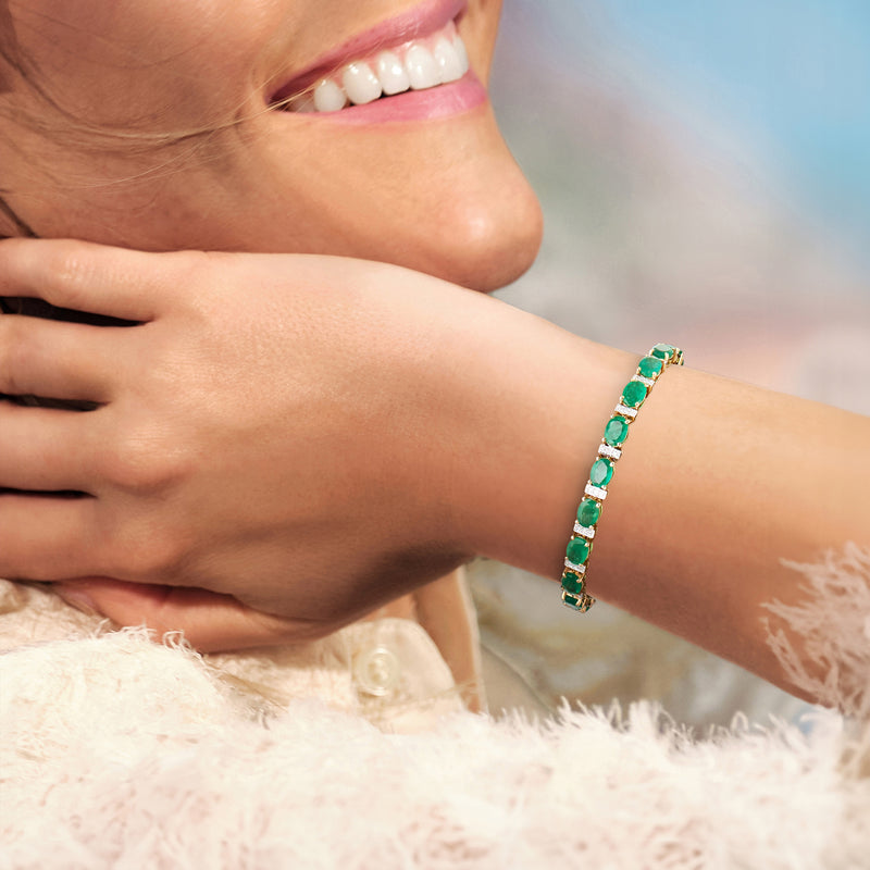 Emerald tennis bracelet with diamond accents on wrist in yellow gold, green stones