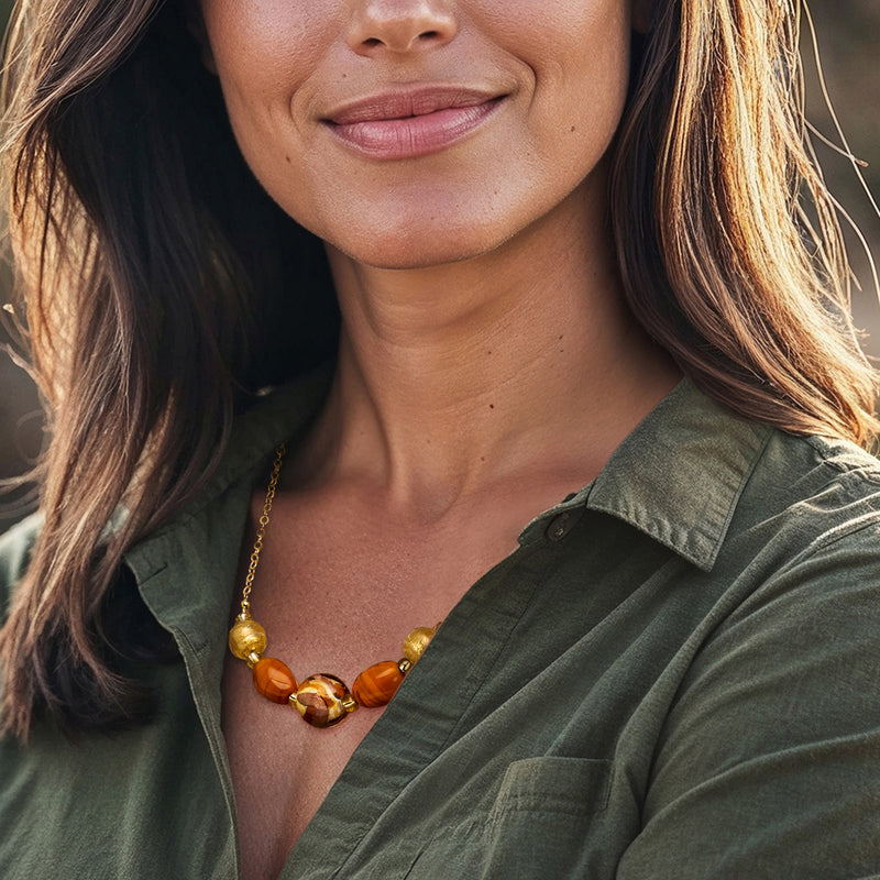 Gold bead necklace with orange and brown glass Murano-style beads on model neckline