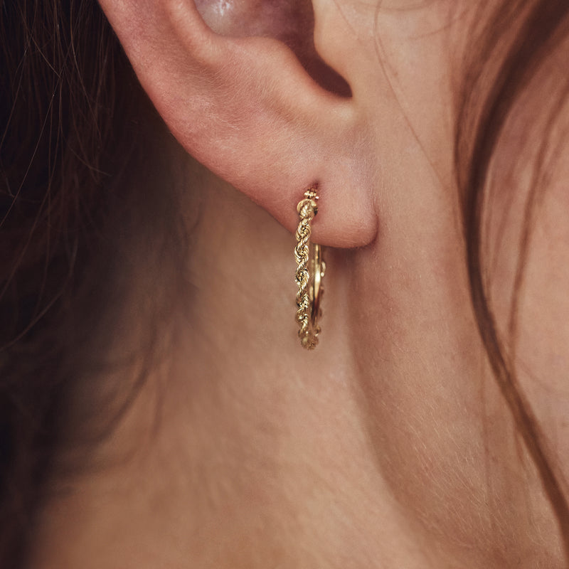 Close-up of yellow gold rope-chain hoop earring with twisted textured links