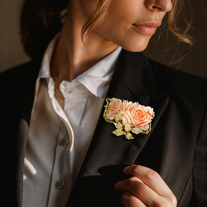 Coral rose gold floral pin worn on blazer lapel, with diamond accents and leaf details
