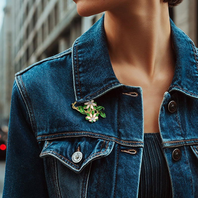 Flower pin with green enamel leaves and pink petals, set with small clear stones on denim