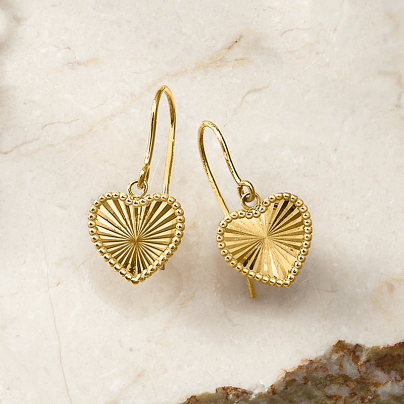 Yellow gold heart sunburst drop earrings, textured heart dangles from earwires.