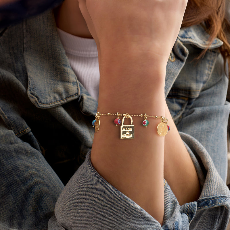 Gold-tone charm bracelet on wrist with multicolored bead charms and padlock centerpiece
