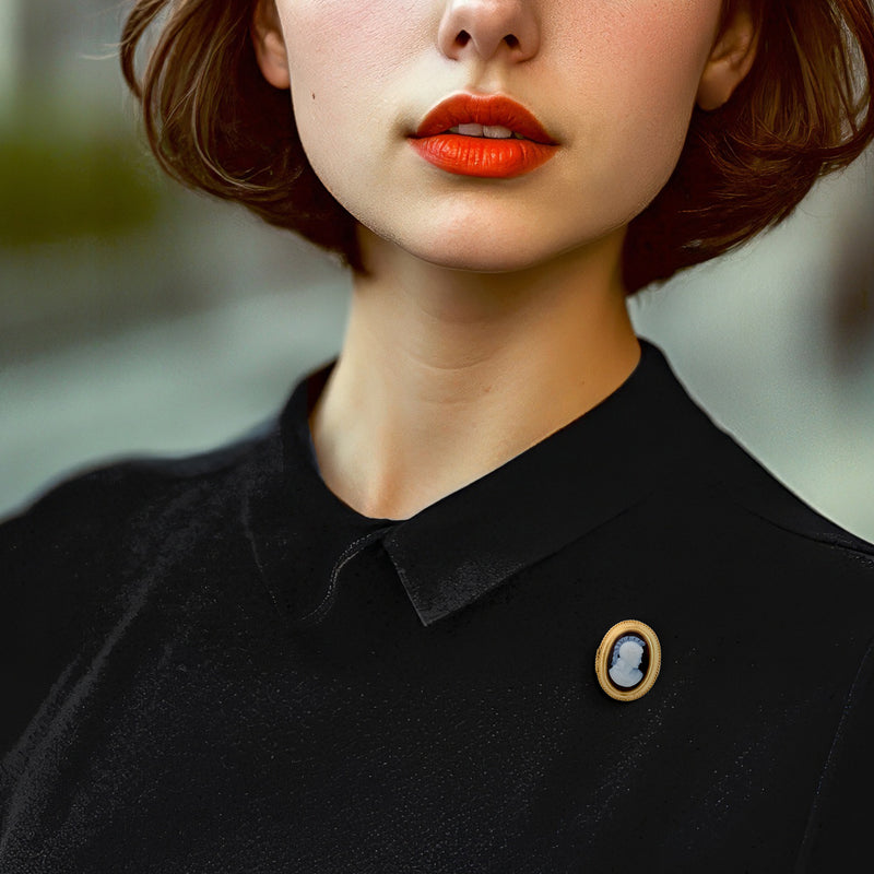 Small oval cameo pin in yellow gold with white profile on dark background, on black shirt