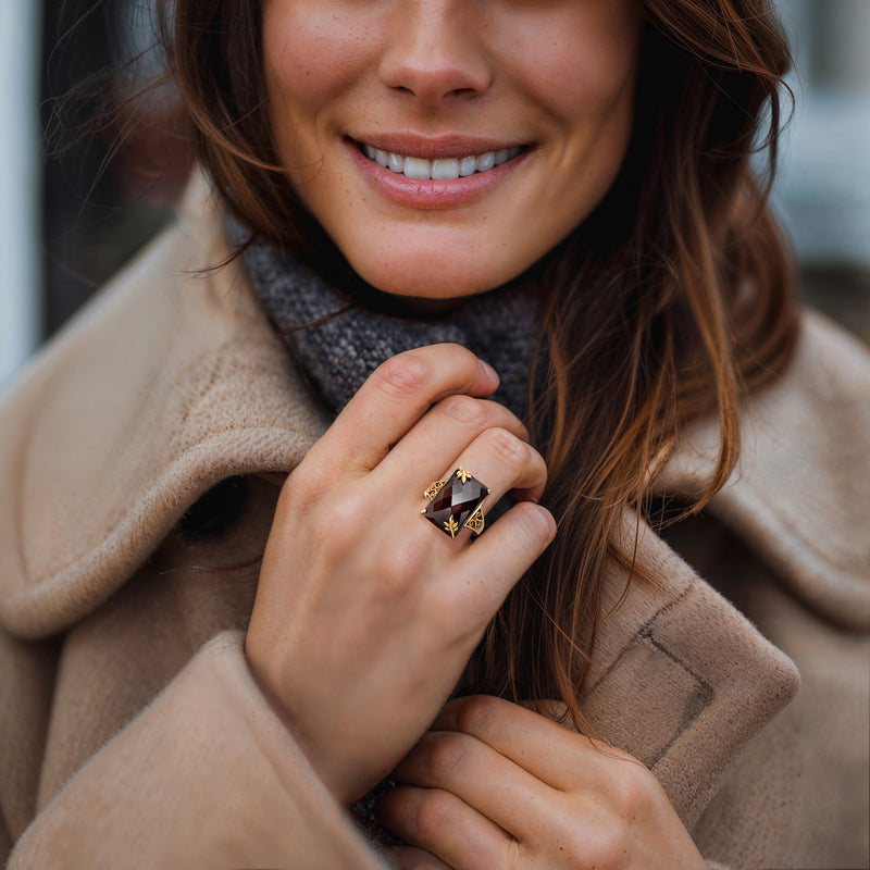 Gold ring with dark smoky quartz center stone and leafy accents on finger