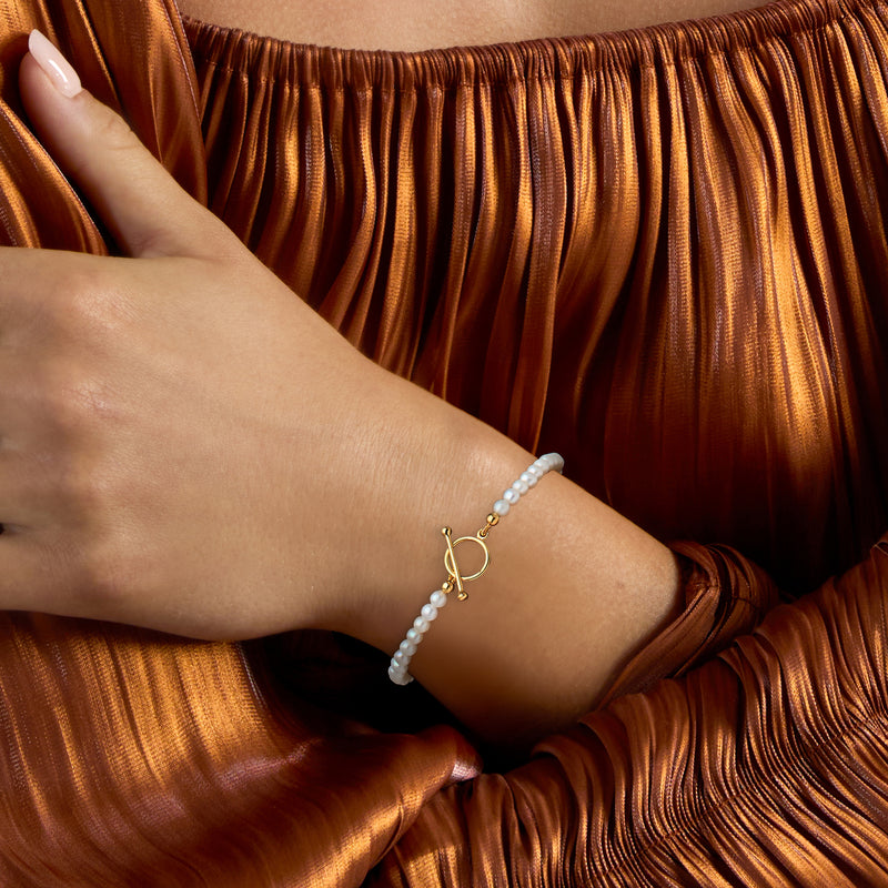 Cultured pearl toggle bracelet worn on wrist with small gold charm clasp