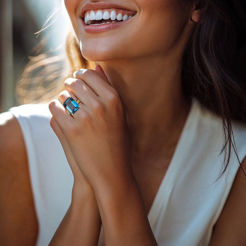 Woman wearing gold over sterling ring with rectangular blue topaz; close-up hand pose