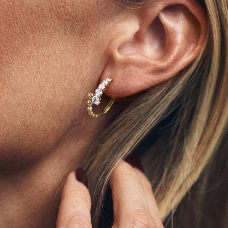 Close-up of gold beaded bypass hoop earring with round diamond-like stones