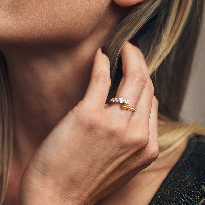 Gold diamond bypass ring on finger with round stones and beaded accents