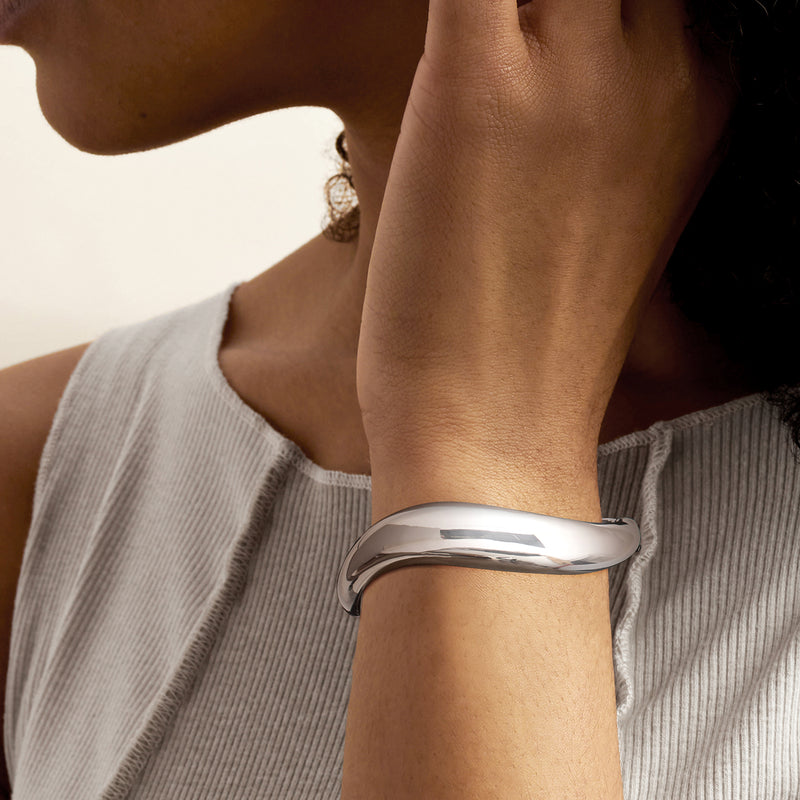 Sterling silver bangle on wrist, smooth oval with reflective sculpted curve